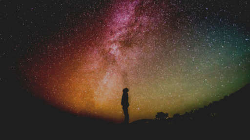 An image of a person looking into a colourful night sky