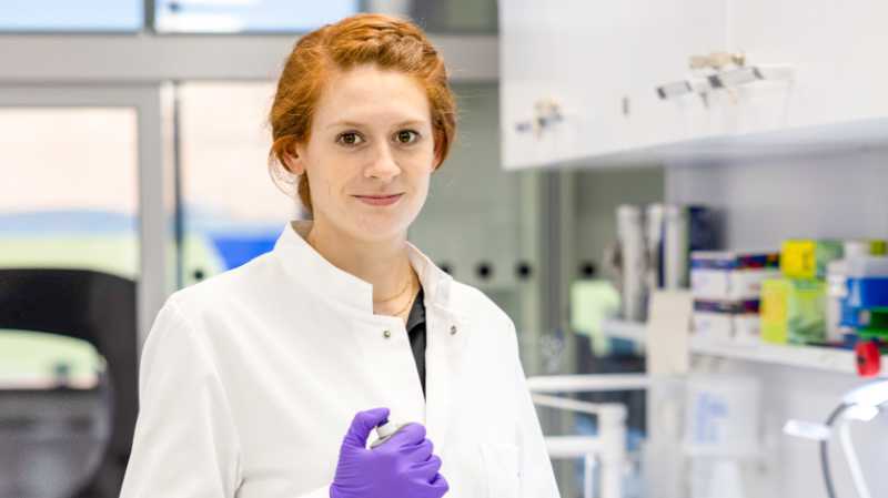 Young scientist in the lab, looking at the camera, wearing a lab coat and holding a pipette
